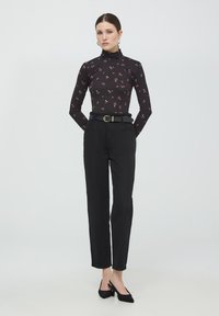 Maglione a collo alto floreale nero abbinato a pantaloni neri a vita alta, fissati con una cintura nera e fibbia dorata, completato da scarpe con tacco nere.