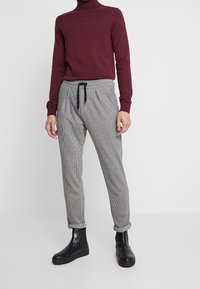 Maglione a collo alto bordeaux, taglio aderente, abbinato a pantaloni grigi a quadri con vita elasticizzata e coulisse. Stivaletti neri completano il look.