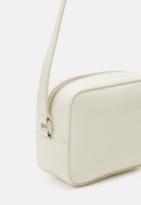 Borsa a mano di colore crema, dal finish lucido e dalla forma rettangolare, con chiusura a zip e tracolla rimovibile. Texture liscia con dettagli di cucitura sui bordi.