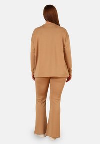 Harmaa loungewear-setti, jossa on pitkähihaiset paita löysällä istuvuudella ja levenevät housut. Tekstuuri on ainutlaatuinen ja malli on yksinkertainen, ilman kuvioita.