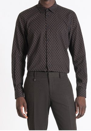 Mand iført en sort skjorte med knapper og et lille geometrisk mønster, kombineret med mørke, skræddersyede bukser.