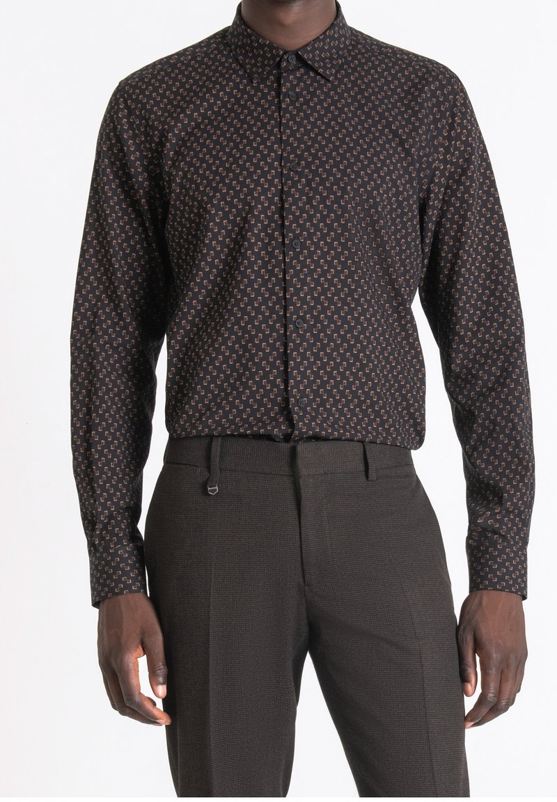 Homme portant une chemise noire à boutons avec un petit motif géométrique, associée à un pantalon sur mesure foncé.