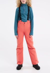 Tepláková fleece bunda na zips v tyrkysovej farbe spárovaná s koralovými snehovými nohavicami, ktoré majú nastaviteľné čierne traky a bočné zipsové vrecká, nosené s čiernymi topánkami.