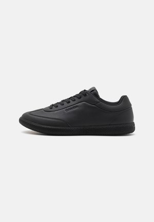 Chaussures de sport noires avec une tige synthétique lisse, une semelle extérieure en caoutchouc texturé et un design classique à lacets, arborant un logo discret sur le côté.