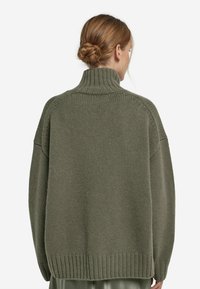 Sweter w oliwkowym kolorze, dziany, z wysokim kołnierzem, opuszczonymi ramionami i ściągaczem. Teksturowany materiał o luźnym kroju.