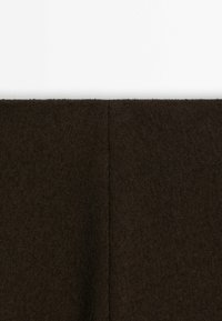 Gros plan d'un tissu texturé marron foncé avec une couture verticale centrale sur un fond uni gris clair.