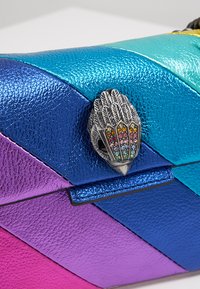 Bolso de mano de cuero sintético multicolor con un patrón de chevron en azul, verde azulado y púrpura, y un cierre decorativo metálico que recuerda a plumas.