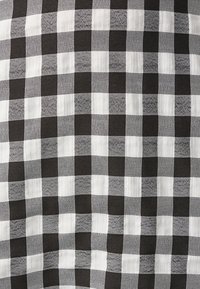 Mustavalkoinen ruudullinen kangas, jossa on kirjavan ruutukuvio, sisältäen kontrastisia nelikulmioiden kokoja tekstuurin ja visuaalisen mielenkiinnon lisäämiseksi.