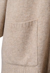 Beżowy sweter wełniany z teksturowanym wykończeniem, ściągaczami na mankietach oraz dużą kieszenią z przodu dla dodatkowego akcentu. Miękka i ciepła tkanina.