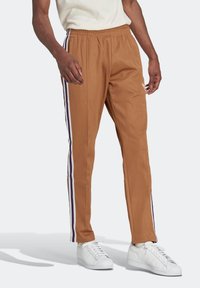 Pantalones de chándal marrones con cintura elástica, con rayas laterales en blanco y púrpura. Confeccionados en una tela suave y ligera.
