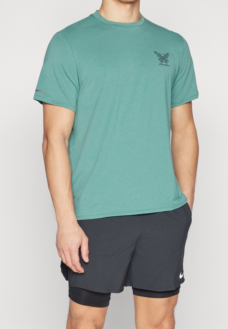 Vaaleansininen lyhythihainen urheilupaita, jossa on teksturoitu kangas. Paidassa on pieni musta logo rinnassa ja kontrastiväriset harmaat yksityiskohdat.