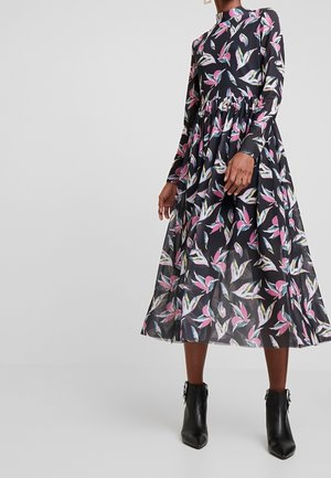 Woman wearing a long-sleeve, high-neck black dress with pink and white floral patterns, paired with black ankle boots with buckles.