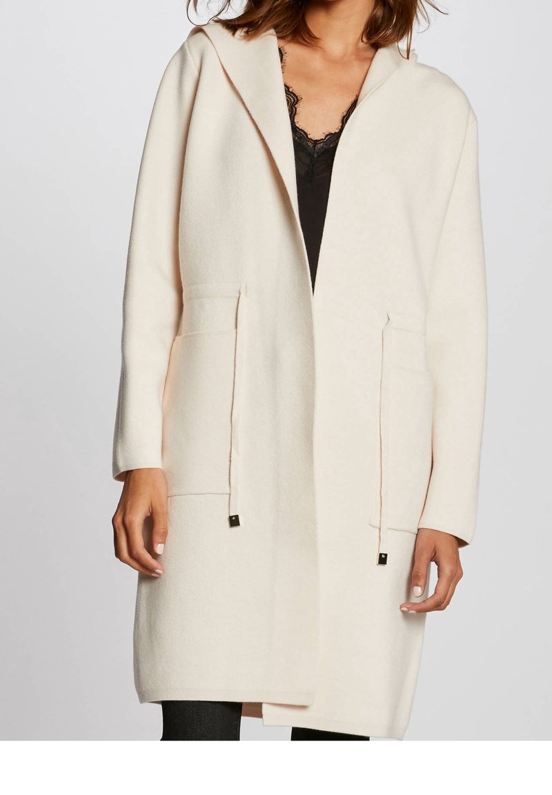 Lichtbeige hooded coat gemaakt van zachte stof, met twee voorzakken en accenten van goudkleurig beslag. Minimalistisch ontwerp met strakke lijnen.