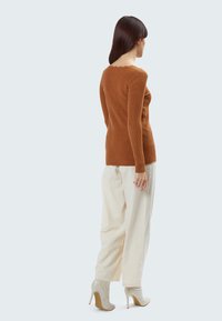 Roestkleurige ribbeltrui met een gegolfde halslijn, gecombineerd met losse beige broek en lichtgrijze haklaarzen.