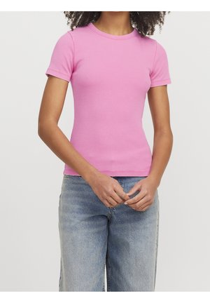 Woman wearing a fitted, short-sleeve pink ribbed t-shirt and light blue high-waisted jeans, standing with hands loosely clasped.