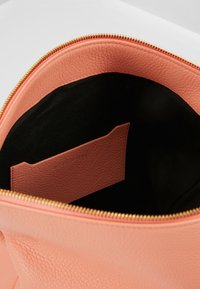 Inuti av en persikofärgad läderhandväska med svart foder, innehållande ett litet kortfack i rosa. Guldzipperdetalj vid öppningen.