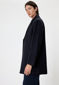 Marineblauwe wollen jas met een getailleerd ontwerp, enkelvoudige knopenrij aan de voorkant, met een notch-kraag en twee zijzakken. Gladde textuur met een strakke silhouet.