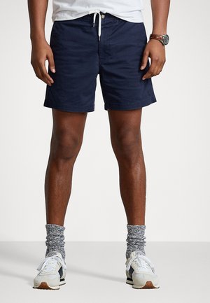 Marineblaue Badehosen mit verstellbarem Bund. Weiße Sneakers mit grauen gemusterten Socken kombiniert. Saum ordentlich und minimales Branding-Detail.