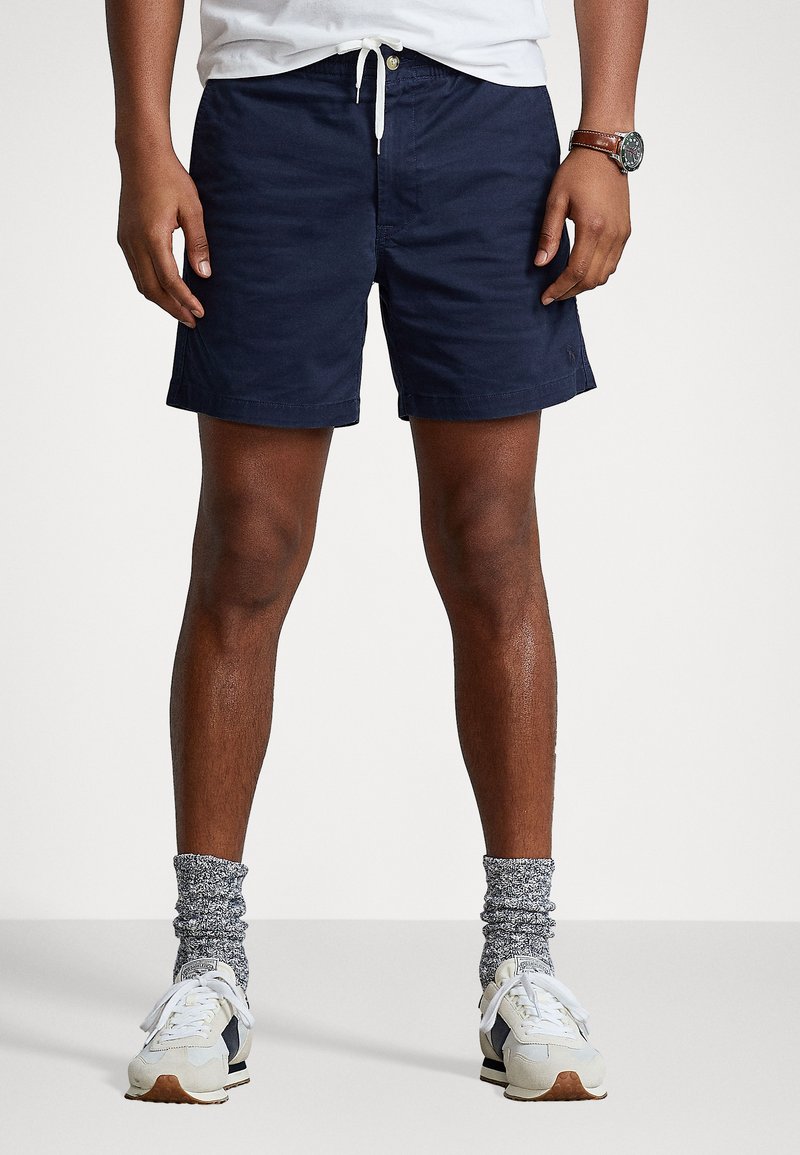 Costumi da bagno blu navy con vita elasticizzata. Abbinamento con sneakers bianche e calze grigie a fantasia. Orlo curato e dettagli di branding minimali.