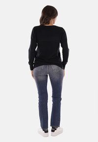Top nero a maniche lunghe con scollatura rotonda, abbinato a jeans blue fitted e sneakers bianche. Tessuto liscio e design semplice.