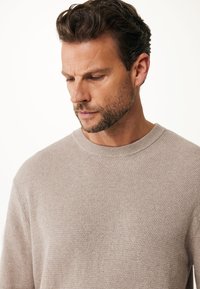 Beige gestrickter Pullover mit einem strukturierten Muster, rundem Ausschnitt und gerippten Bündchen. Weicher Stoff mit subtilen Farbvariationen.