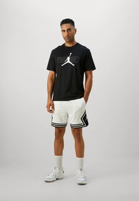 Mustast puuvillast t-särk, millel valge graafilise logoga disain, kombineeritud valgete võrgukangast lühikeste pükstega, millel mustad detailid ja küljes triibud. Valged sportlikud tossud.