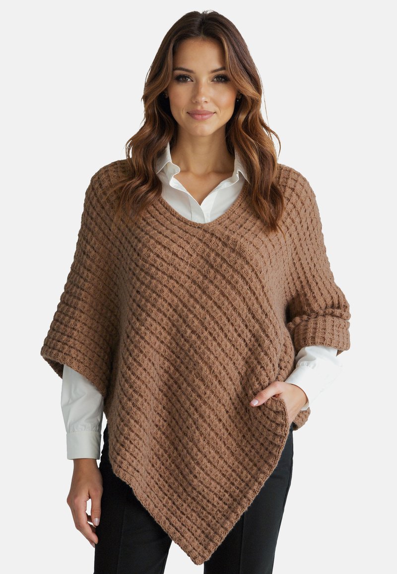 Poncho intrecciato marrone con un motivo testurizzato diagonale, scollo a V, maniche arrotolate e una tasca frontale, indossato sopra una camicia bianca.