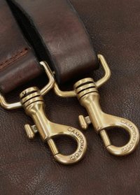 Bronzen metalen sluitingen met veerbelaste haken, bevestigd aan donkerbruine leren banden. Op het beslag is de tekst "CAMPOMAG" gegraveerd.