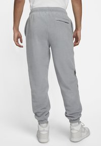 Joggers grises de felpa con cintura elástica, bolsillos laterales y puños acanalados. Un bolsillo trasero presenta un detalle de costura plana. Combinados con zapatillas blancas.