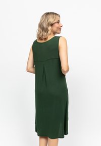 Grünes ärmelloses Kleid mit Rundhalsausschnitt, weichem Stoff, Falten-Detail am Rücken und einer fließenden Silhouette, die bis zur Mitte der Wade reicht.