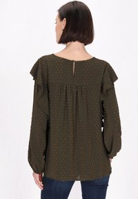 Oliwkowa bluzka z falbankami na rękawach, w kropki, zaokrąglonym dekoltem, z detalem w postaci dziurki na plecach oraz lekkim marszczeniem poniżej karczka.