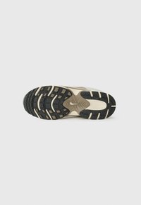 Nike sneakersåle i svart og beige, med en teksturert overflate, multidireksjonal grep og innfelte logo detaljer.