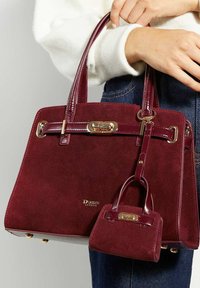 Burgundy suede handbag with polished leather accents, dual handles, and a small matching bag attached, featuring gold hardware and logo detail.
