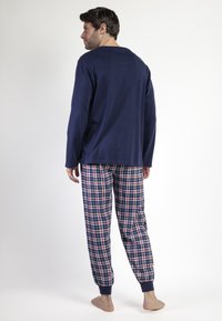 Camisa de manga larga azul marino combinada con pantalones de cuadros que presentan líneas rojas y azules, puños elásticos y un ajuste holgado.
