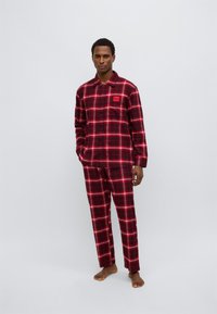 Σετ πιτζάμας με κόκκινο και μαύρο καρό, κατασκευασμένο από απαλό ύφασμα, με πουκάμισο με κουμπιά και τσέπη στο στήθος και μπαντζάκια που ταιριάζουν.