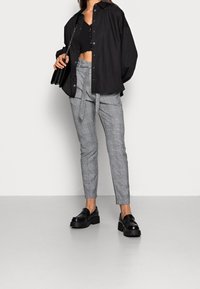 Black oversized shirt, cropped black top, checkered gray trousers with a tie belt, and black platform loafers. Patterned and layered design.