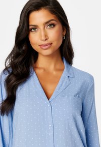Jasnoniebieska koszula z guzikami, zdobiona białymi kropkami, z kieszonką na piersi, kołnierzykiem w stylu notch oraz długimi rękawami o miękkiej teksturze.