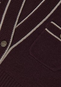 Cardigan tricotat de culoare mov închis, cu margini bej, modele texturate, butoane decorative din bronz și un mic buzunar pe piept.