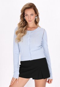 Cárdigan de manga larga azul claro con un escote en forma de ola, que presenta patrones verticales y botones en forma de perla, combinado con una falda corta negra.