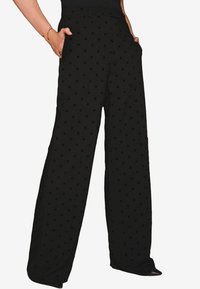 Pantaloni neri a gamba larga con pois neri a rilievo, dotati di tasche laterali e vita aderente, realizzati in un tessuto leggero.
