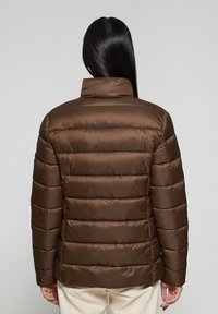 Brązowa kurtka puchowa z wysokim kołnierzem, poziomym pikowaniem i błyszczącą teksturą. Rękawy są dopasowane i mają miękkie wykończenie.