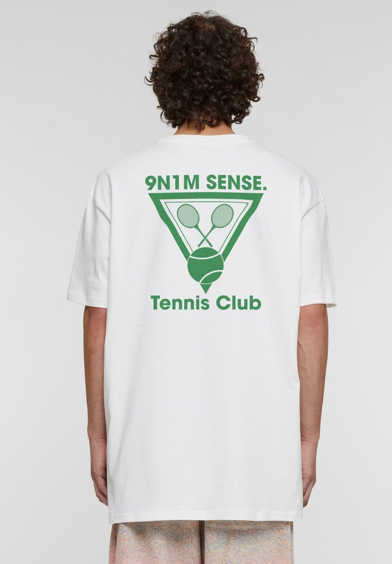 Balts īsām piedurknēm T-krekls ar aizmugurē izsistītu zaļu grafiku, kurā attēloti tenisa racketi un bumba, ar uzrakstu "Tennis Club".