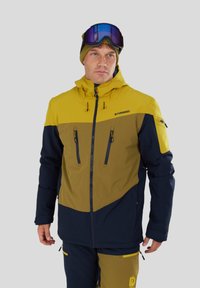 Giacca da sci impermeabile con pannello superiore giallo e pannello inferiore verde oliva, con maniche blu navy. Include due tasche frontali con zip e un cappuccio.