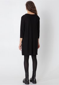 Svart tunikaklänning med trekvartslånga ärmar, gjord av ett mjukt och lätt tyg, med en lös passform och sidfickor.