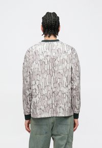 Košeľa s dlhým rukávom z mäkkej, vzorovanej tkaniny s abstraktným sivobielym dizajnom. Ukončená zeleným golierom a manžetami.