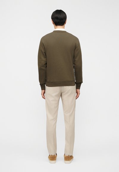 Φούτερ σε ελιά πράσινο με ριμπ μανσέτες και τελείωμα, συνδυασμένο με ανοιχτό μπεζ καλοραμμένο παντελόνι. Το σύνολο ολοκληρώνουν παπούτσια σνίκερς σε ταμπά χρώμα.