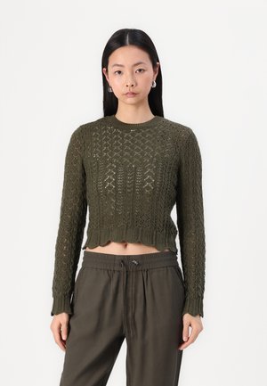 Strikket, cropped sweater i mørk olivengrøn med et tekstureret diamantmønster og bølgekant. Matchet med matchende mørke bukser.
