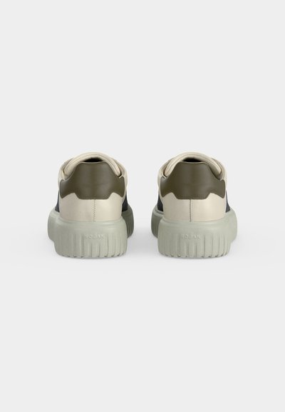 Paire de baskets blanches et vert olive vues de dos, avec semelles épaisses côtelées et col rembourré sur un fond uni.