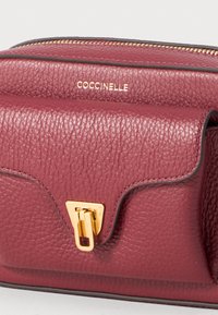 Burgundy leather bag with textured finish, gold hardware clasp, and embossed logo. Rectangular shape with a secure zip closure and contrasting edges.