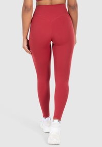 Hooggewaisted leggings in een diep rood, gemaakt van glad, rekbaar materiaal met een naadloos ontwerp en minimale stiknaden.